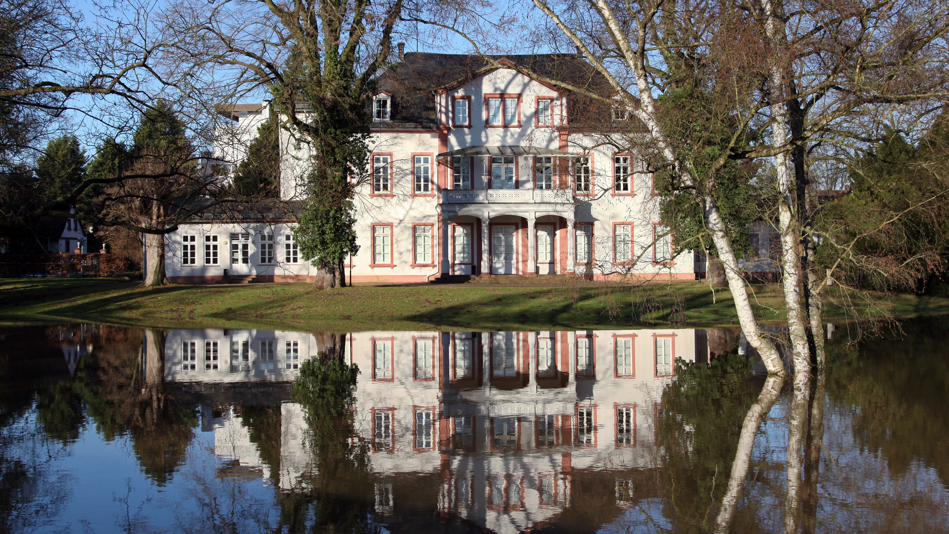 A photo of the exterior of a large, luxury home with a flooded front yard.