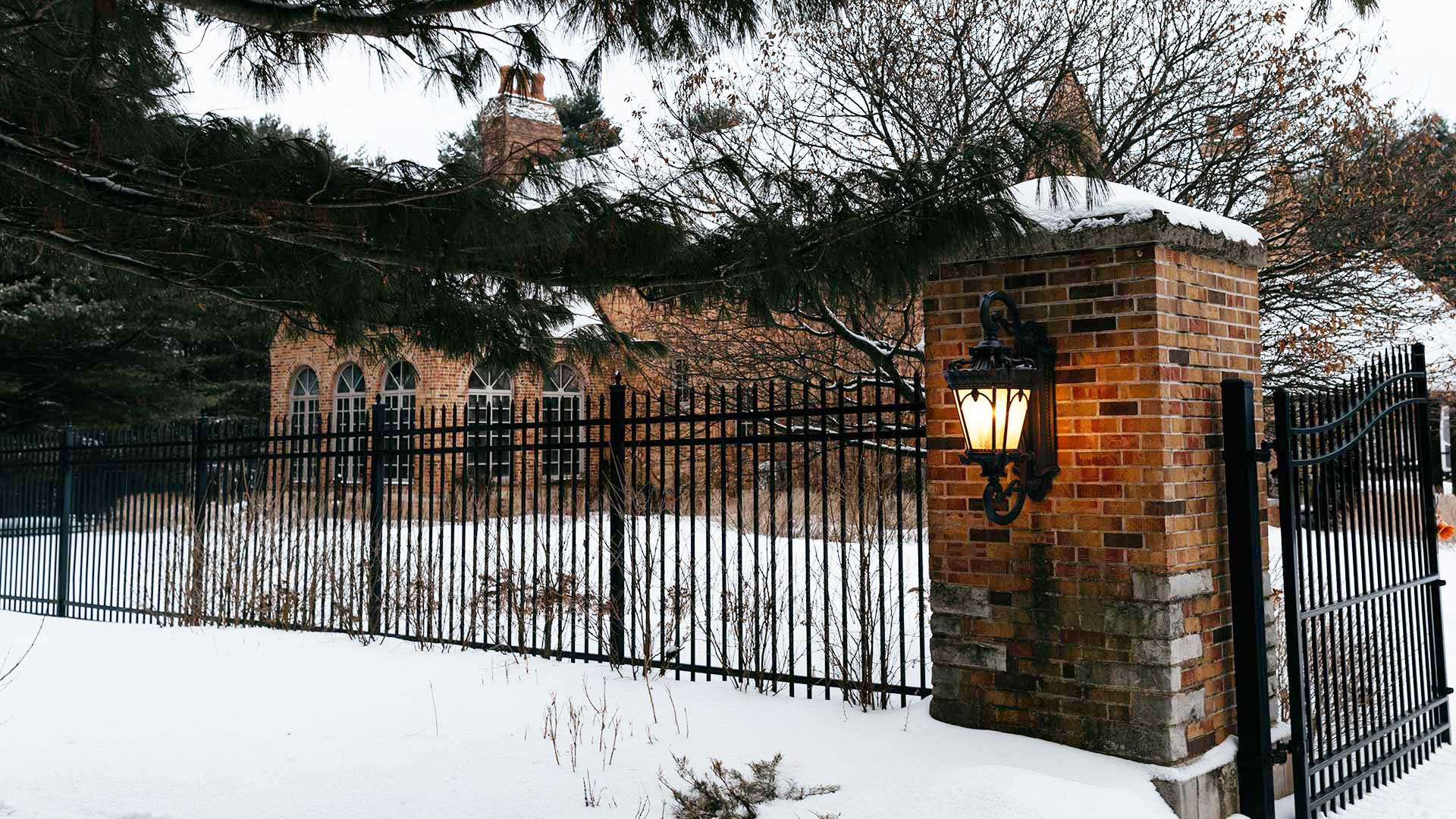 A photo of the front gate of a large brick home with snow on the ground.