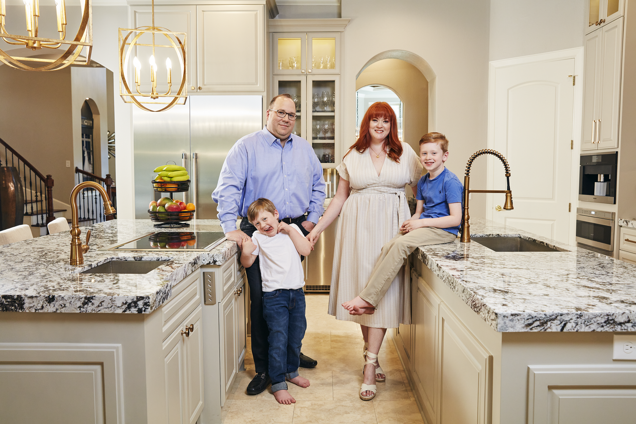 A couple and their two kids posing for a photo standing in-between their kitchen islands.
