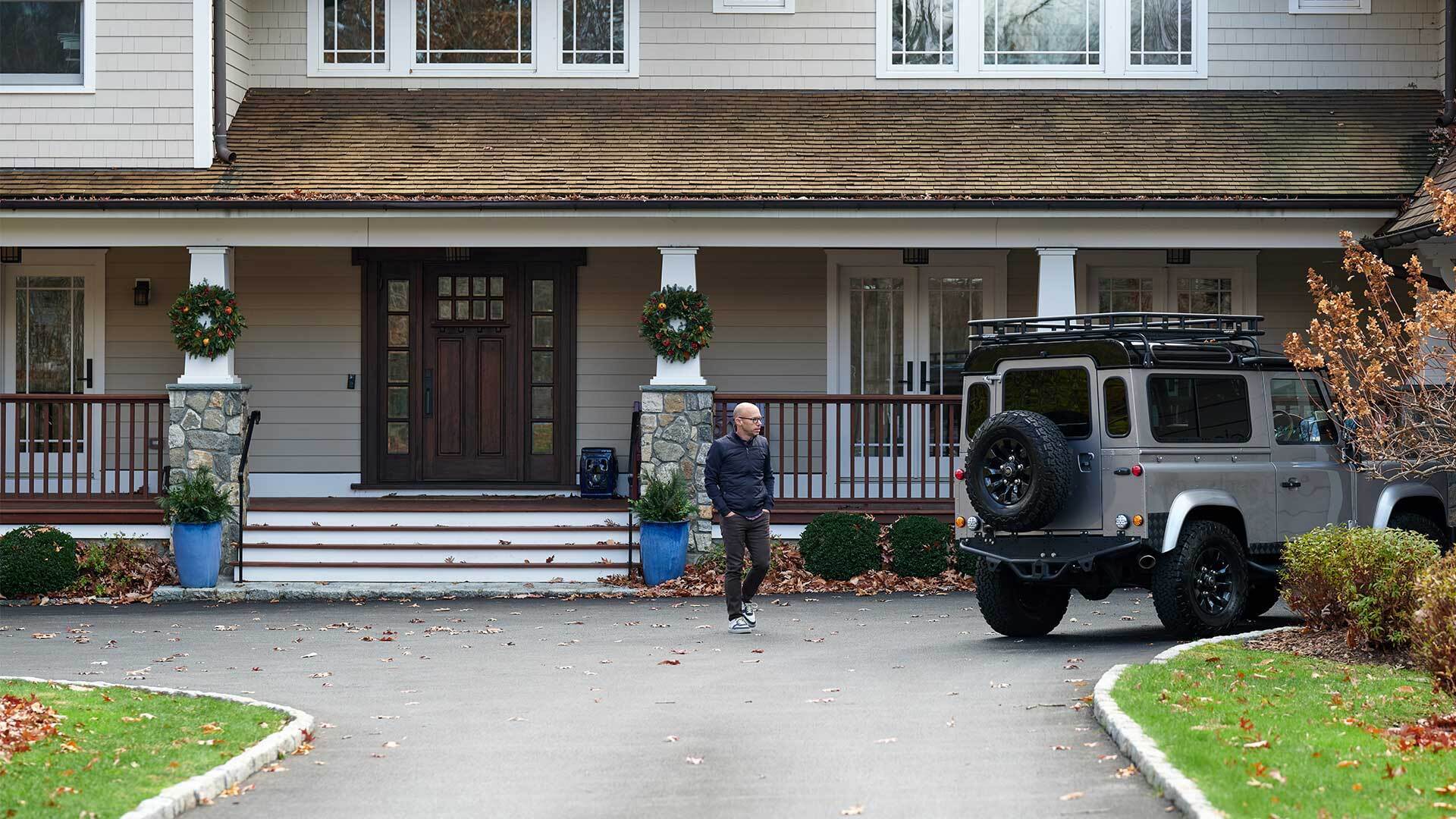 A man in front of a large house, walking toward an SUV.
