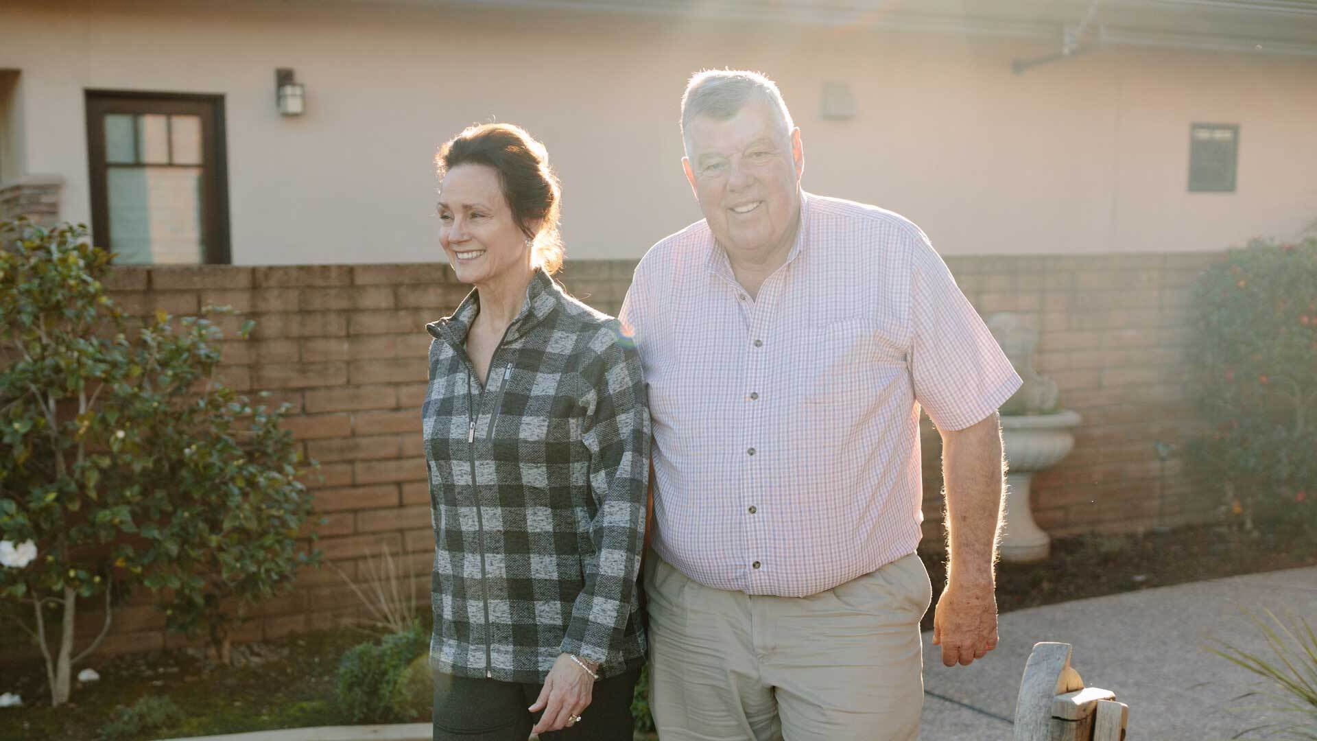 A photo of a smiling couple walking together outside their home.
