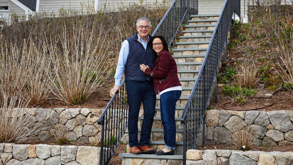A photo of a distinguished looking couple standing on the front steps of their home.