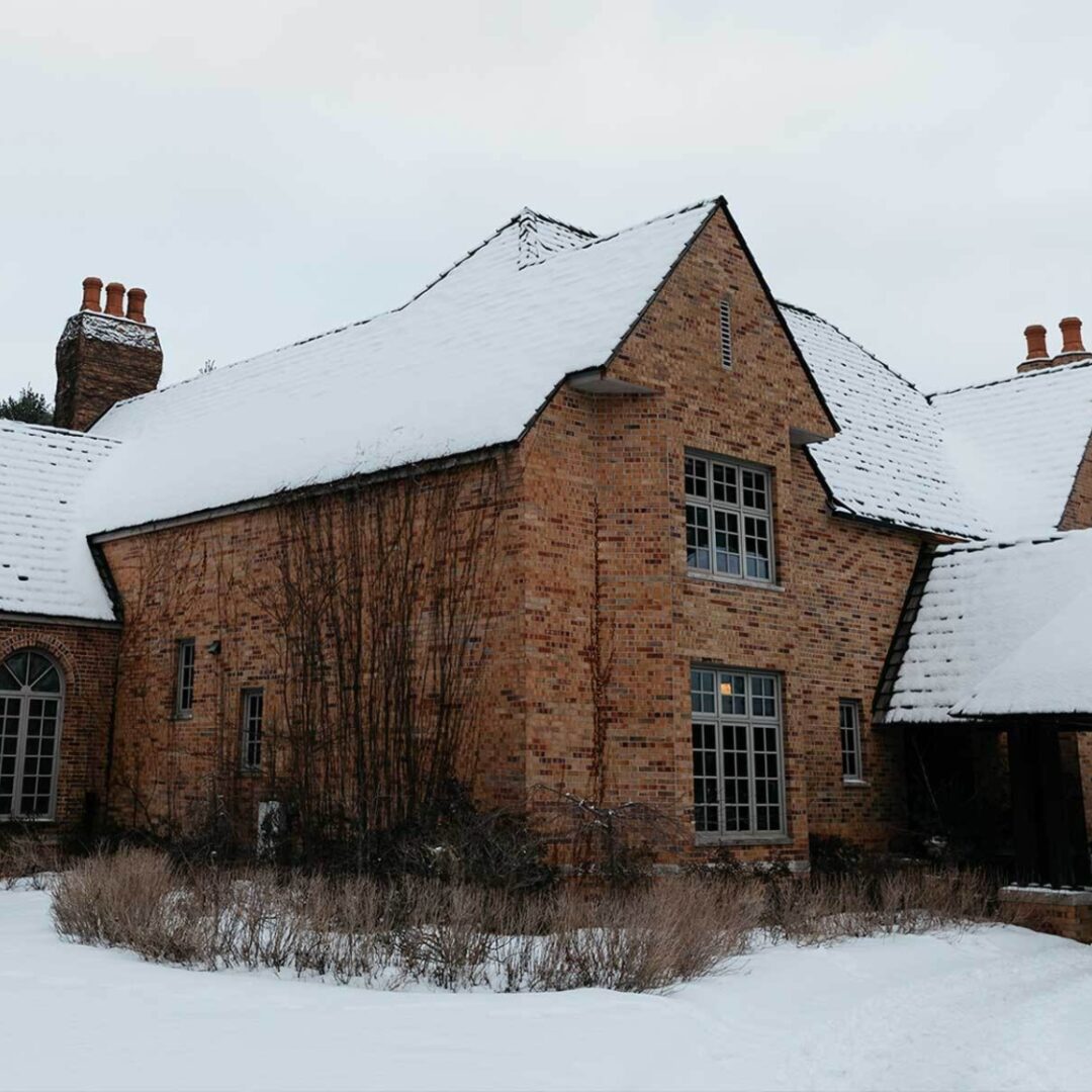 A photo of the exterior of a large, brick home covered in snow.