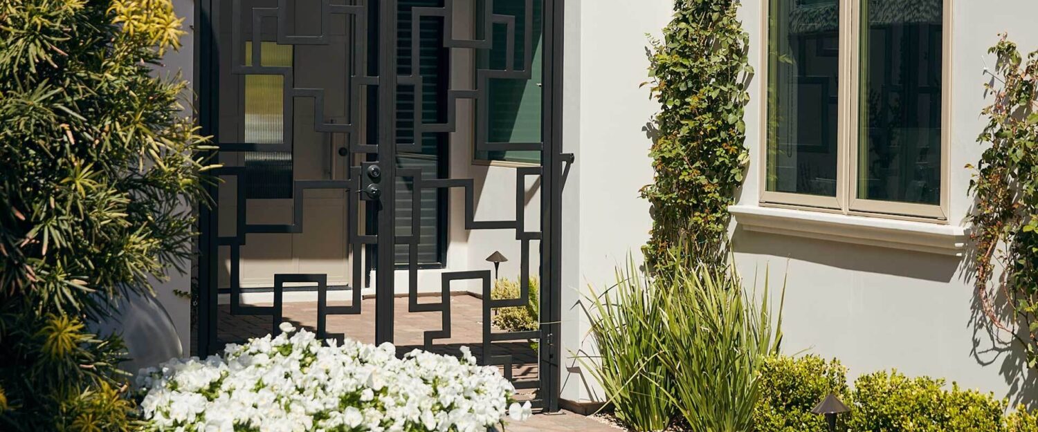 Black, metal front door of a white house behind green shrubs and white flowers