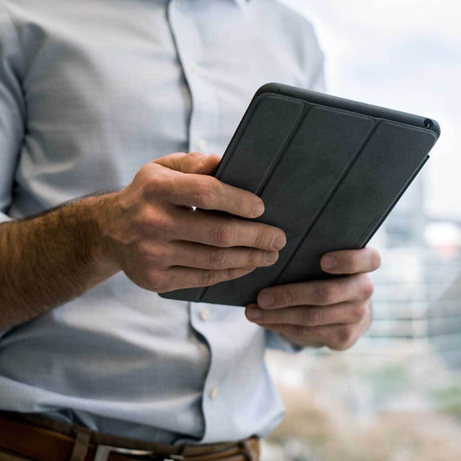 A closeup photo of a man outdoors holding a tablet in his hands.