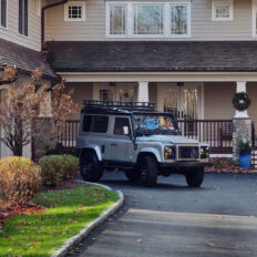 A photo of a customized rugged SUV parked in front of a large home
