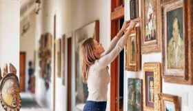 A photo of a woman adjusting a painting on the wall of a large home gallery.