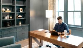 A photo of a man working at a laptop in a large, bright home office.