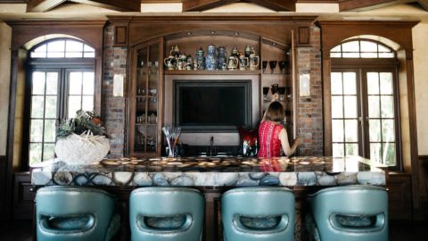 A photo of a woman putting away glasses in a luxurious home bar.