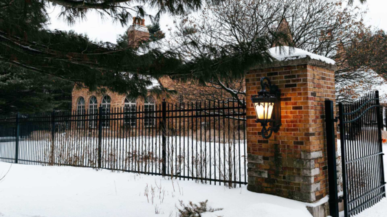 A photo of the front gate of a large brick home with snow on the ground.