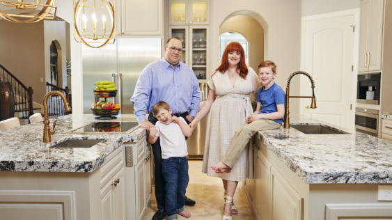 A couple and their two kids posing for a photo standing in-between their kitchen islands.