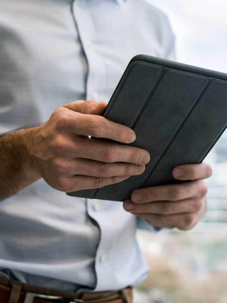 A closeup photo of a man outdoors holding a tablet in his hands.