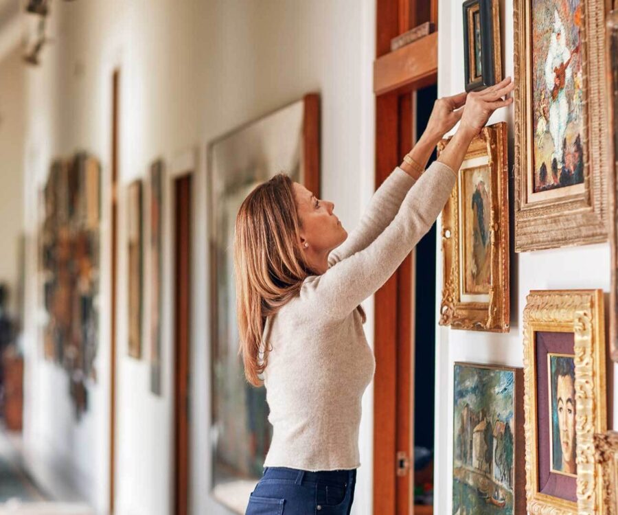A photo of a woman adjusting a painting on the wall of a large home gallery.