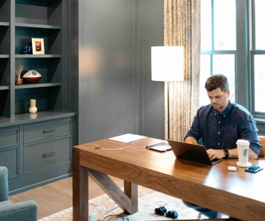 A photo of a man working at a laptop in a large, bright home office.