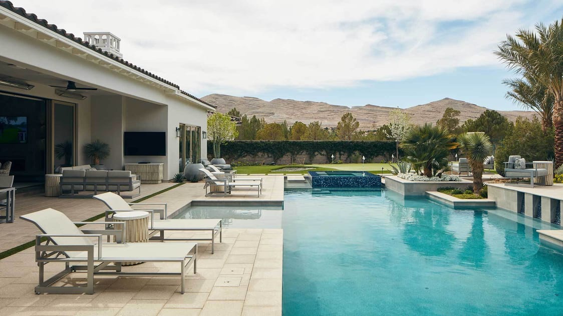 A manicured backyard in the western united states with a large in-ground pool surrounded by trees and white lounge chairs
