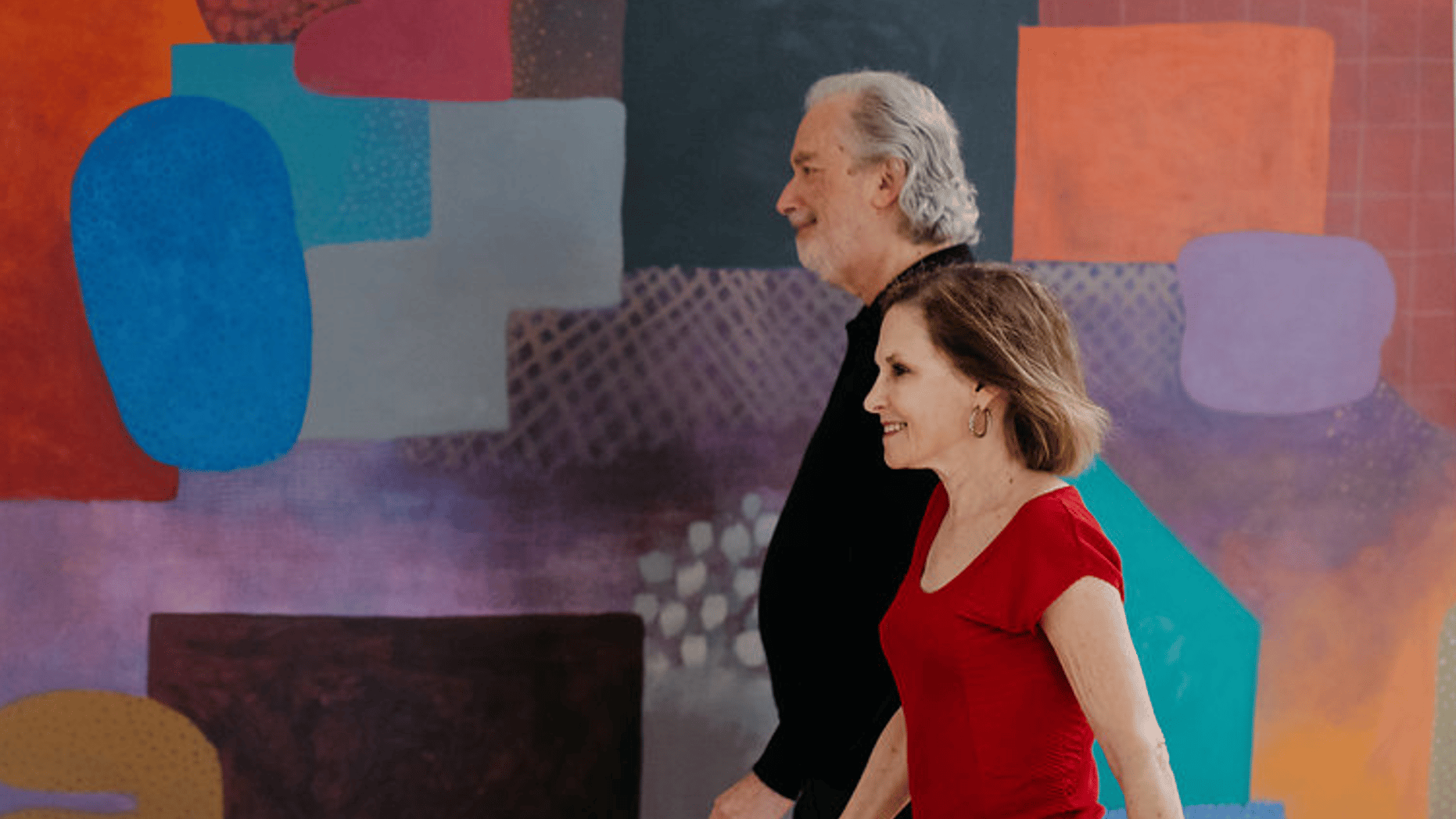 A photo of a couple walking past a large painting