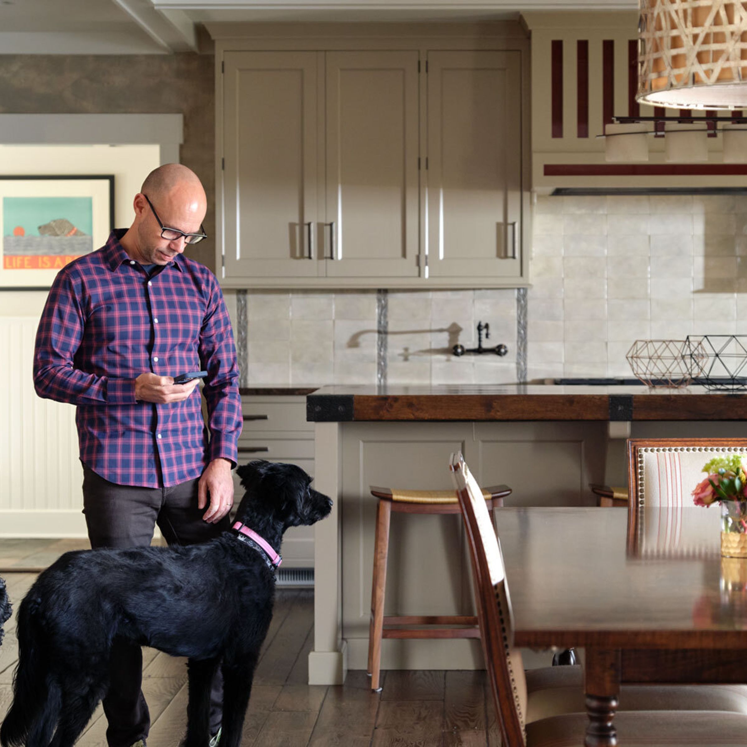 A photo of a man using his cellphone in a large luxurious kitchen.