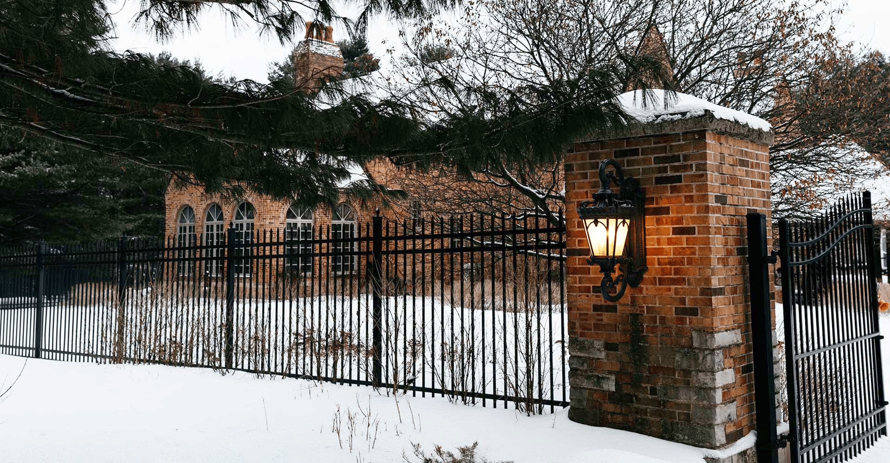A photo of the front gate of a large brick home with snow on the ground.
