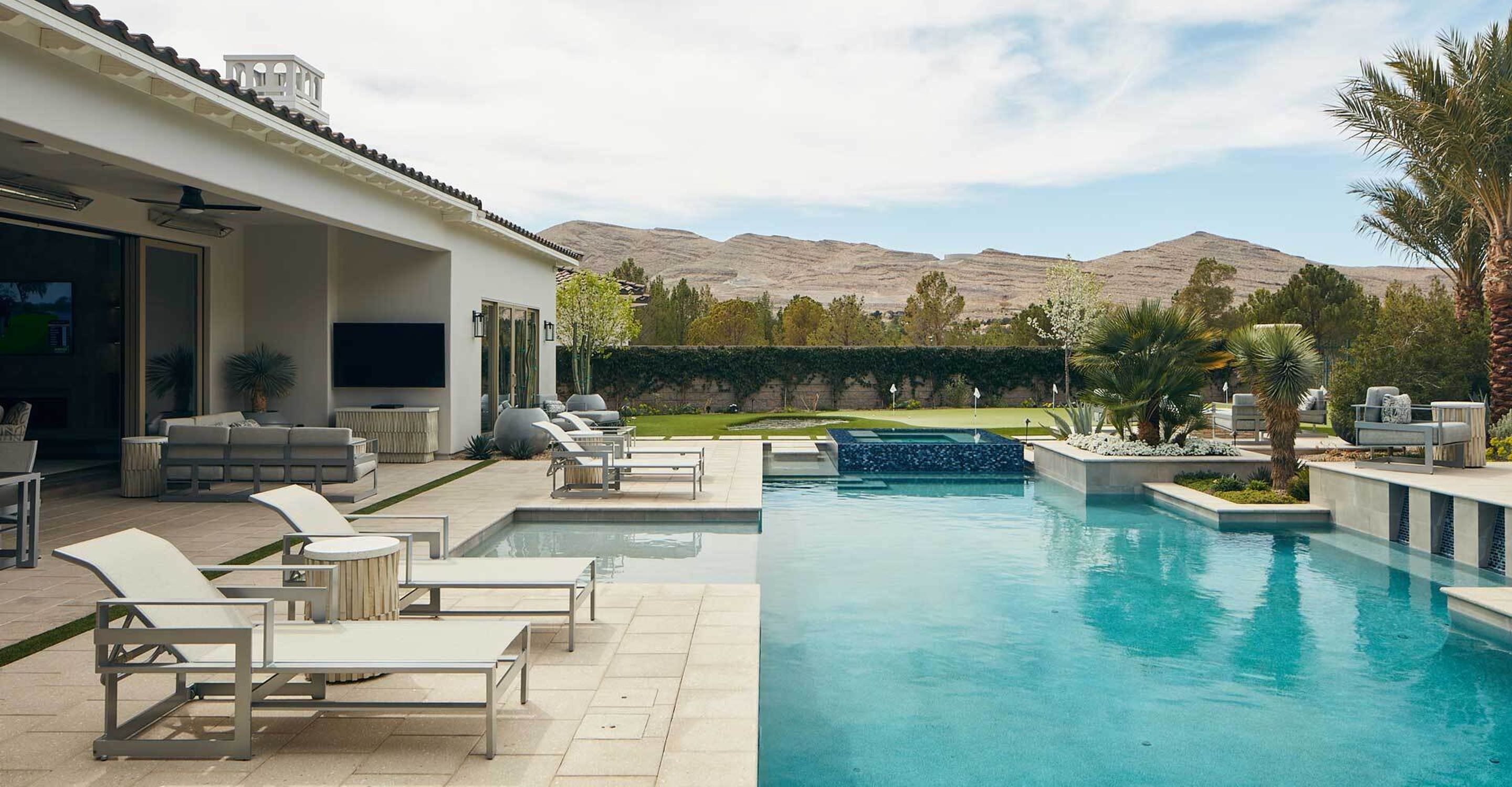 A manicured backyard in the western united states with a large in-ground pool surrounded by trees and white lounge chairs