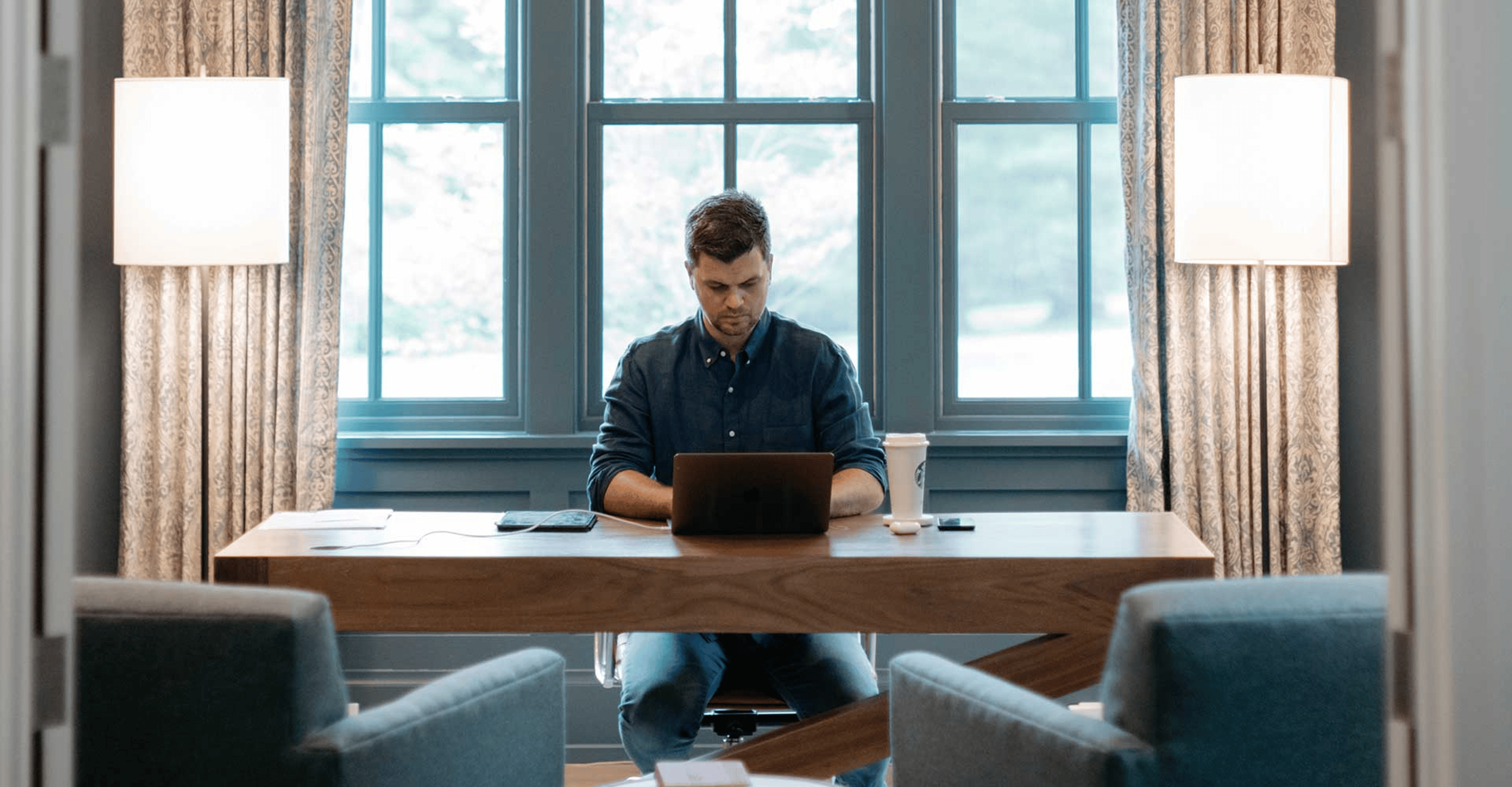 A photo of a man on his laptop in a large, well decorated home office.