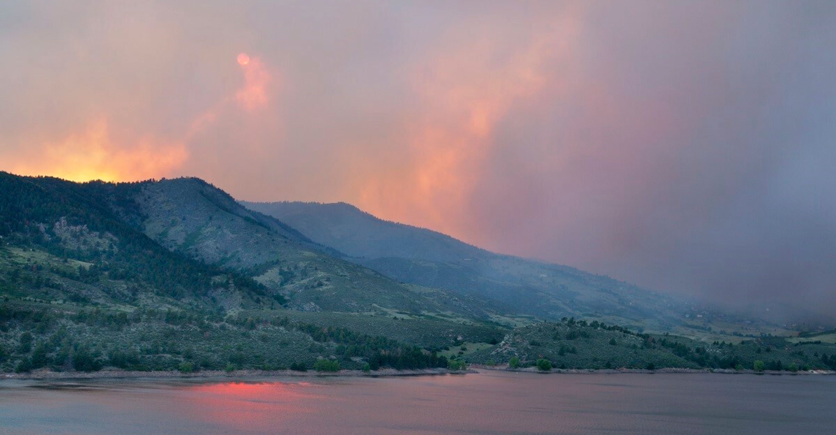 A landscape photo of distant hills with smoke coming off of them