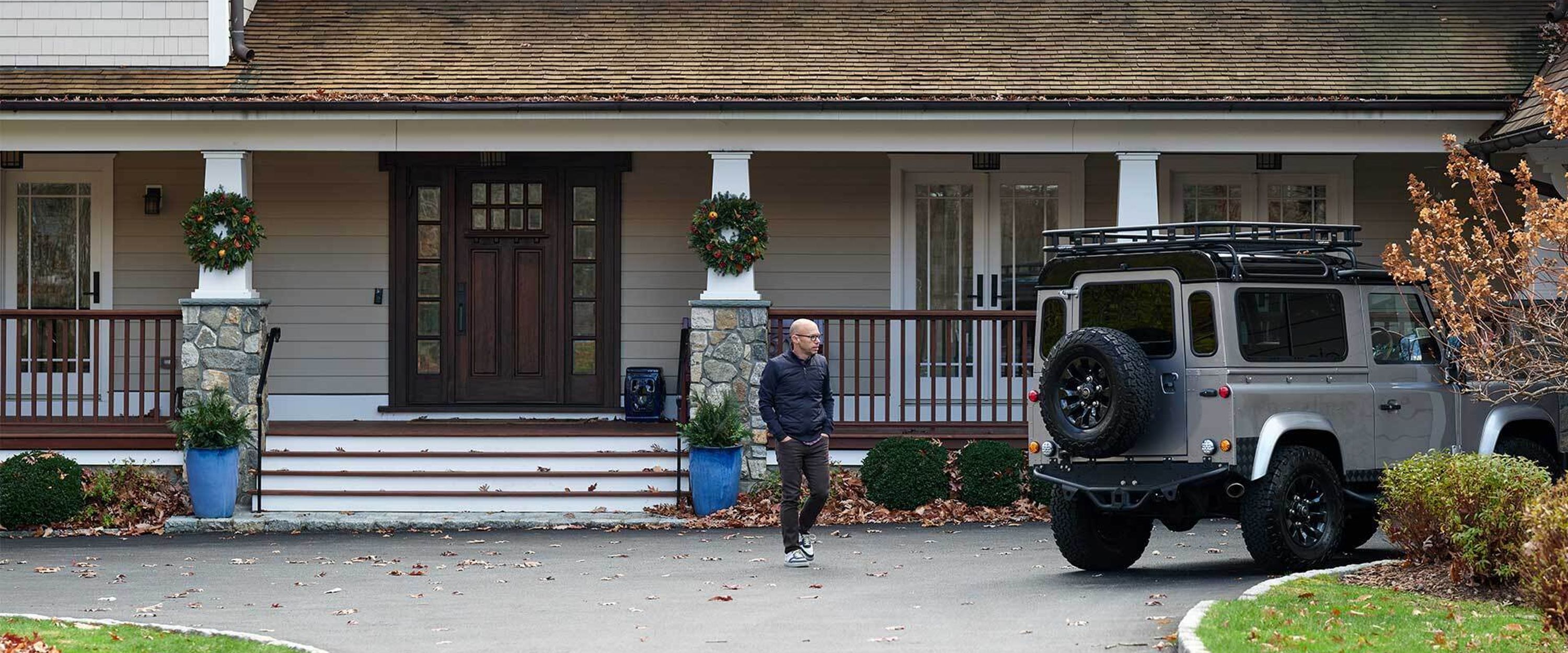 A man in front of a large house, walking toward an SUV.