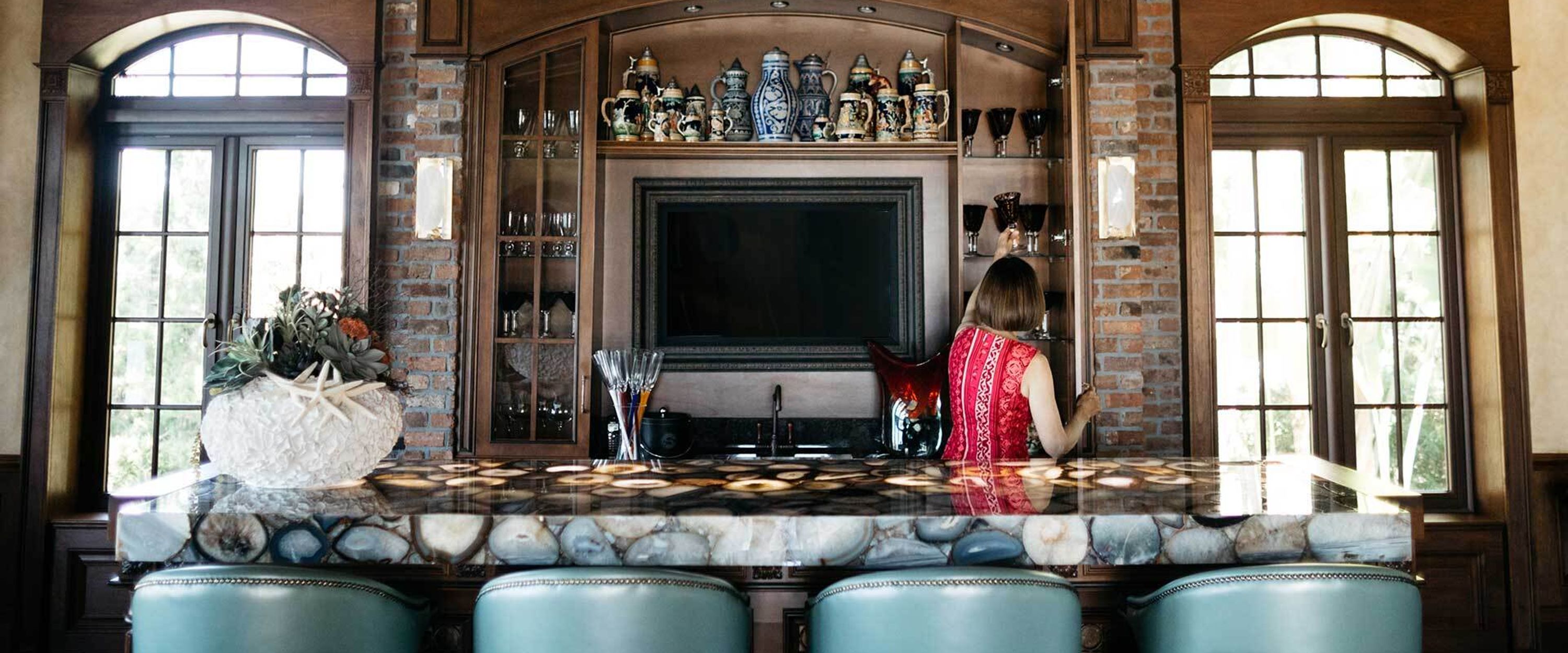 A photo of a woman putting away glasses in a luxurious home bar.